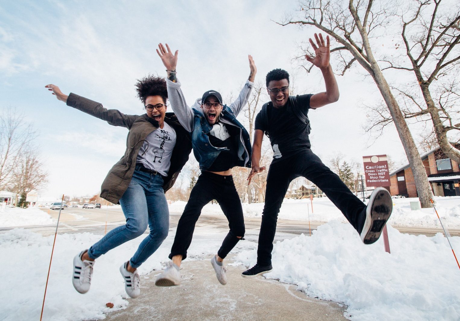 photo of three men jumping on ground near bare trees during daytime